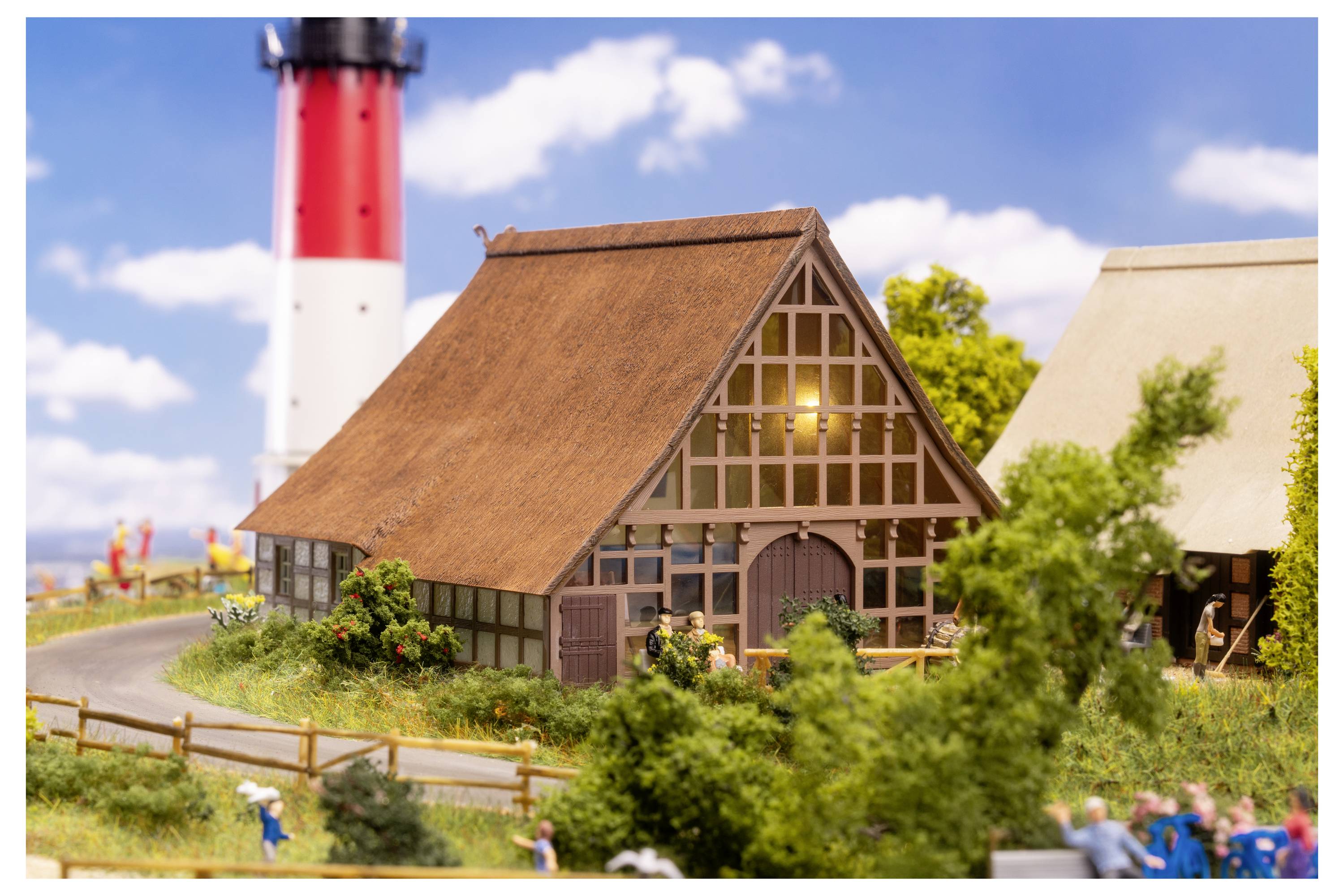Miniaturale Landszene mit einem Haus mit Strohdach neben einem gewundenen Weg, rotweiß gestreiftem Leuchtturm im Hintergrund und kleinen Figuren sowie Bäumen im Vordergrund.