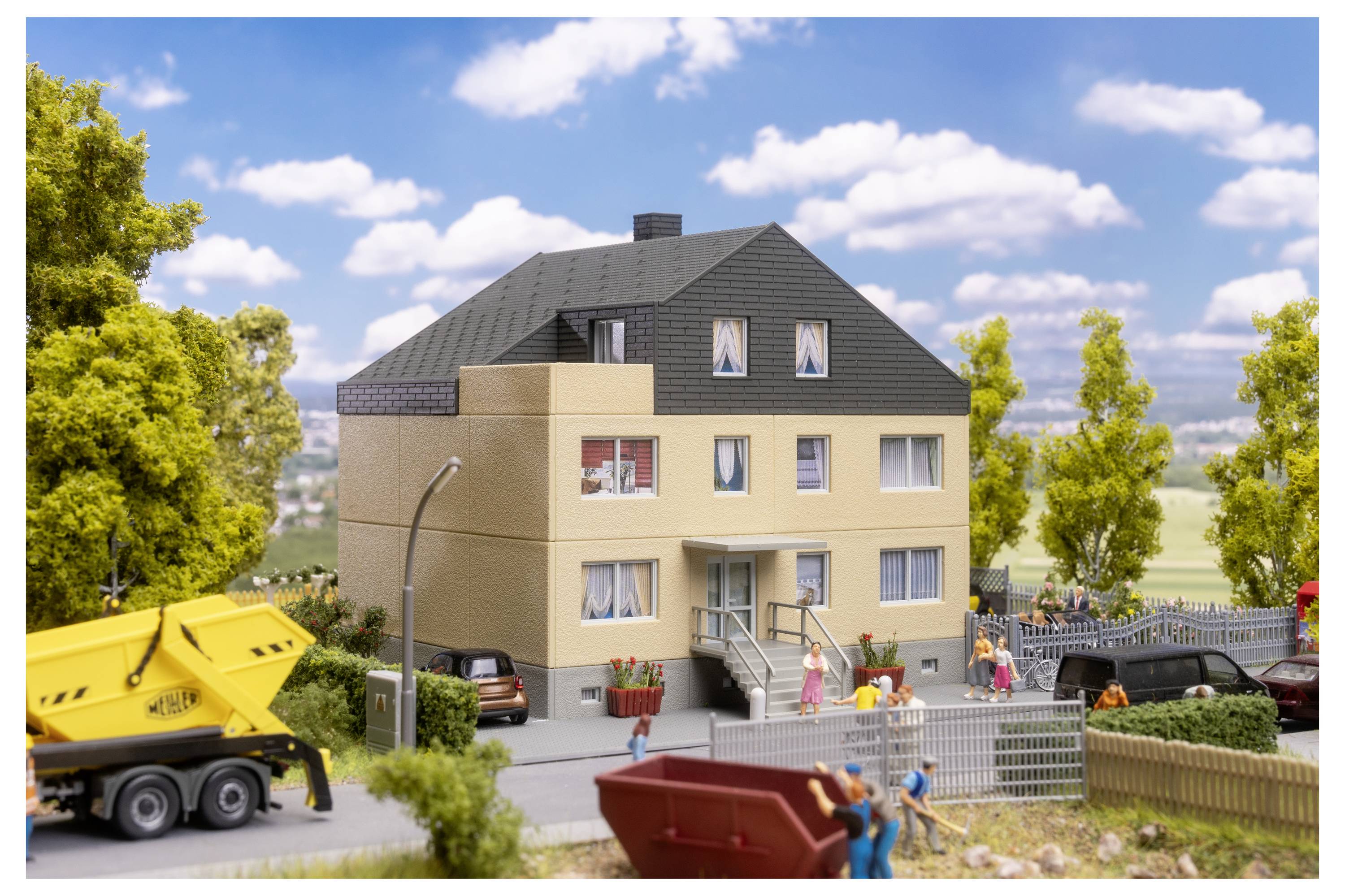 Miniaturszene eines Wohngebiets mit einem beigen Apartmentgebäude, geparkten Autos, Arbeitern und einem gelben Kipper unter blauem Himmel.