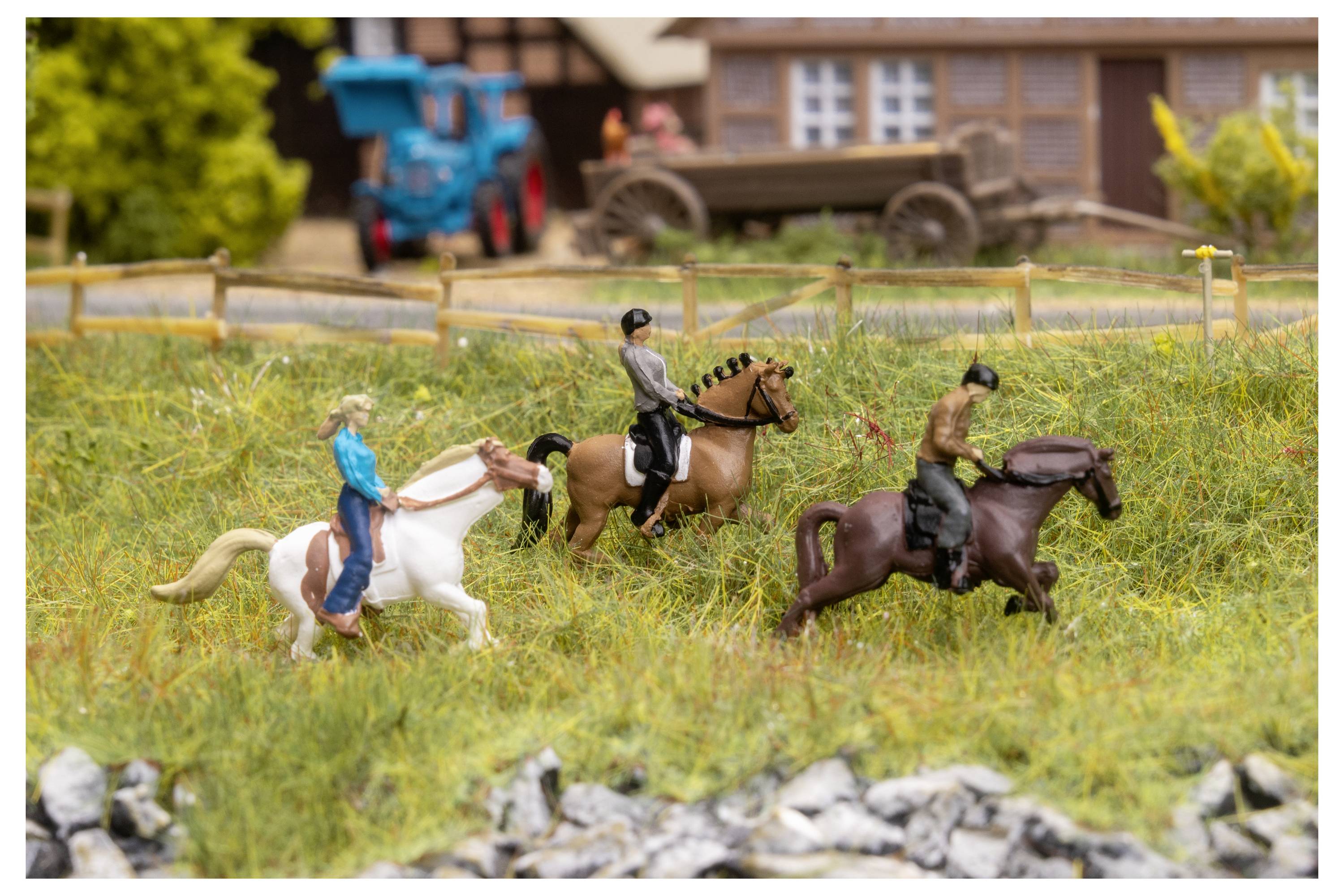 Miniaturszene mit drei Reitern auf Pferden in einem grasbewachsenen Feld, mit einem Zaun und Farmgebäuden im Hintergrund.