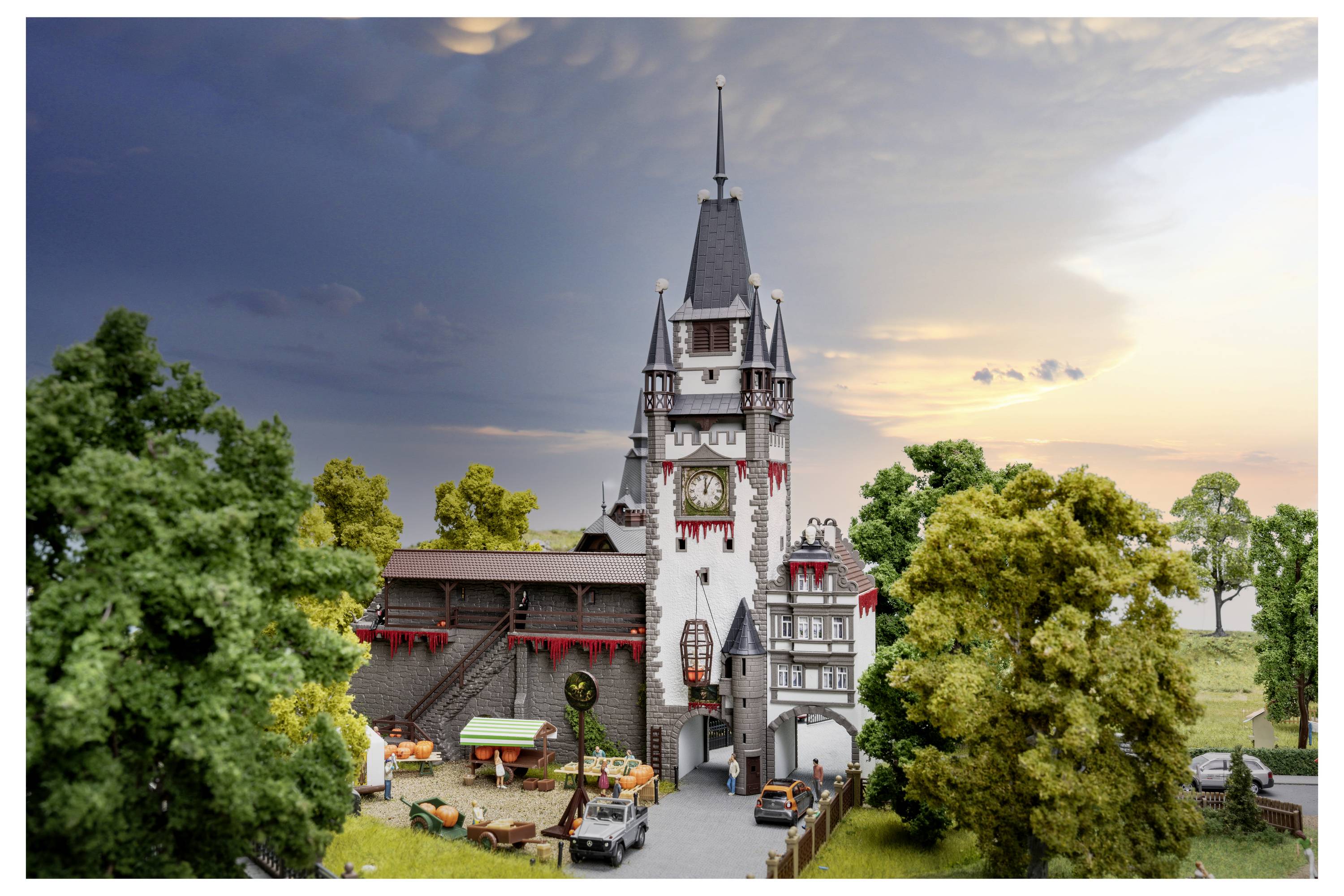 Ein detailliertes Miniaturmodell eines schlossähnlichen Gebäudes mit einem hohen Turm, umgeben von Bäumen und kleinen Figuren bei Sonnenuntergang.