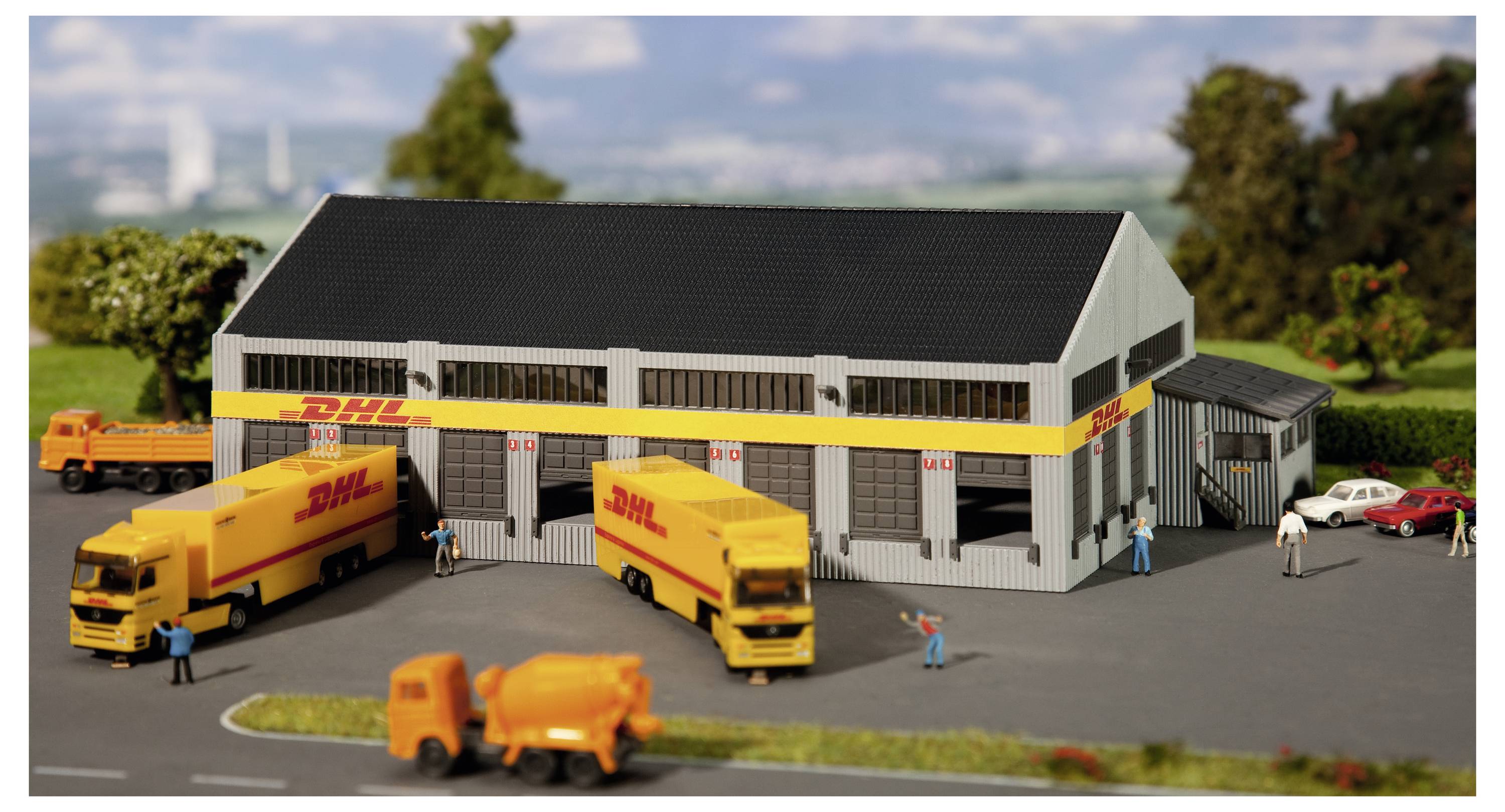 Miniatur-DHL-Logistikdepot mit mehreren gelben Lieferwagen, Arbeitern, einem Tankwagen und geparkten Autos vor einem Lagerhausgebäude.
