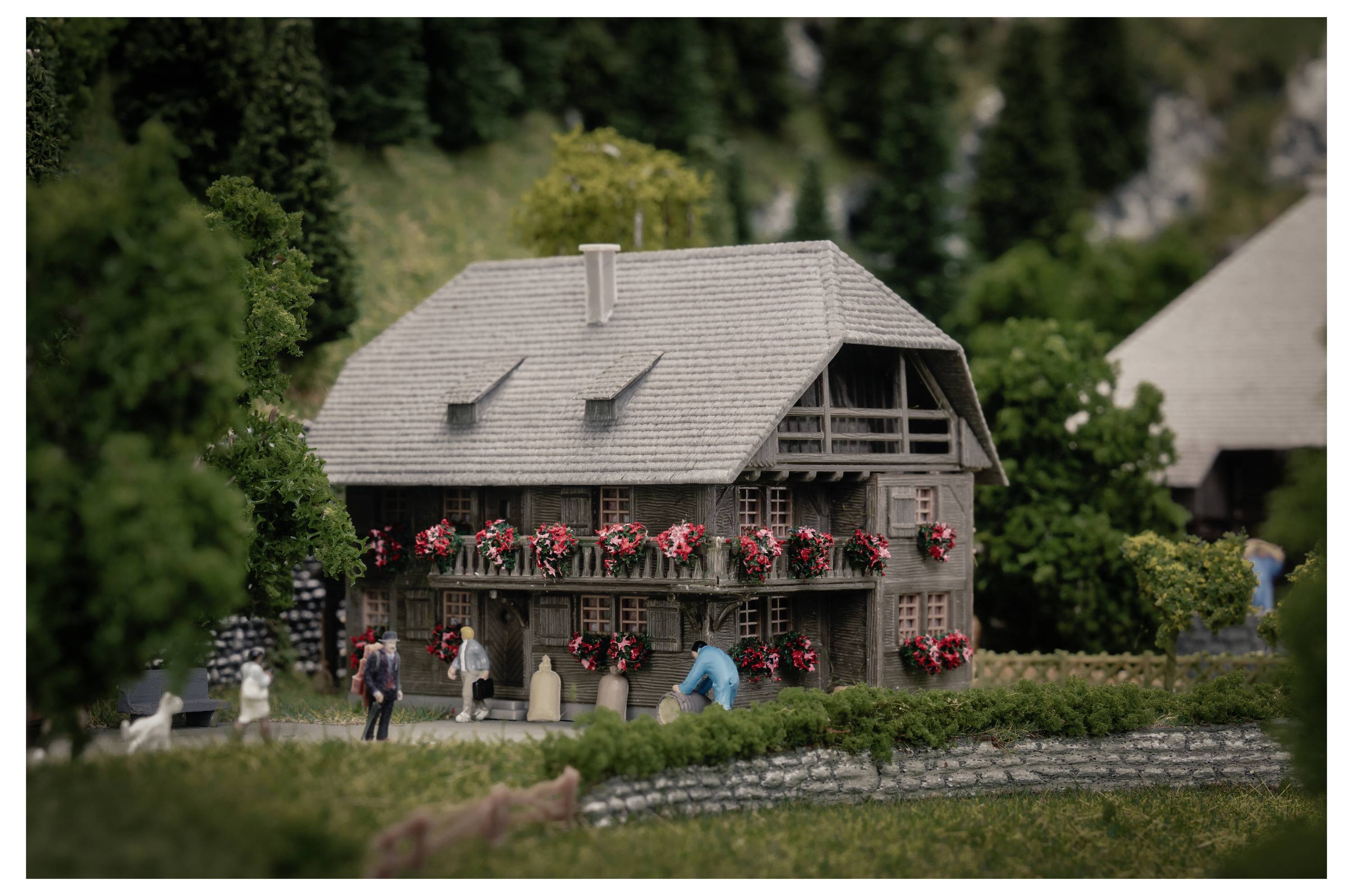 Ein Miniaturmodell eines blumengeschmückten Hauses mit winzigen Menschen in einer landschaftlich gestalteten Dorfszene.