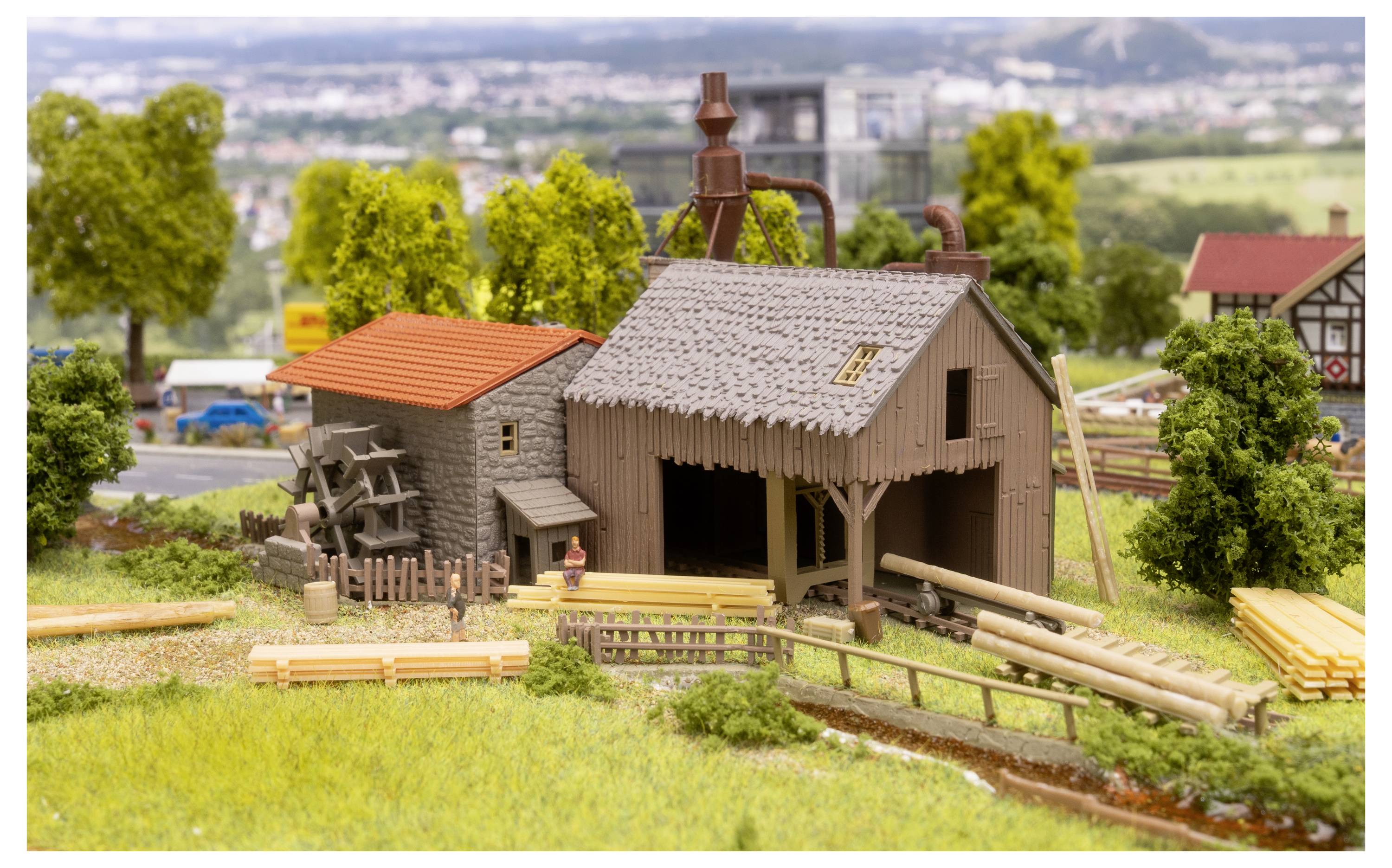 Miniatur-Landszene einer ländlichen Farm mit einer Scheune, einem kleinen Schuppen, Zäunen, gestapeltem Holz und Modellbäumen in einem gestalteten Diorama.