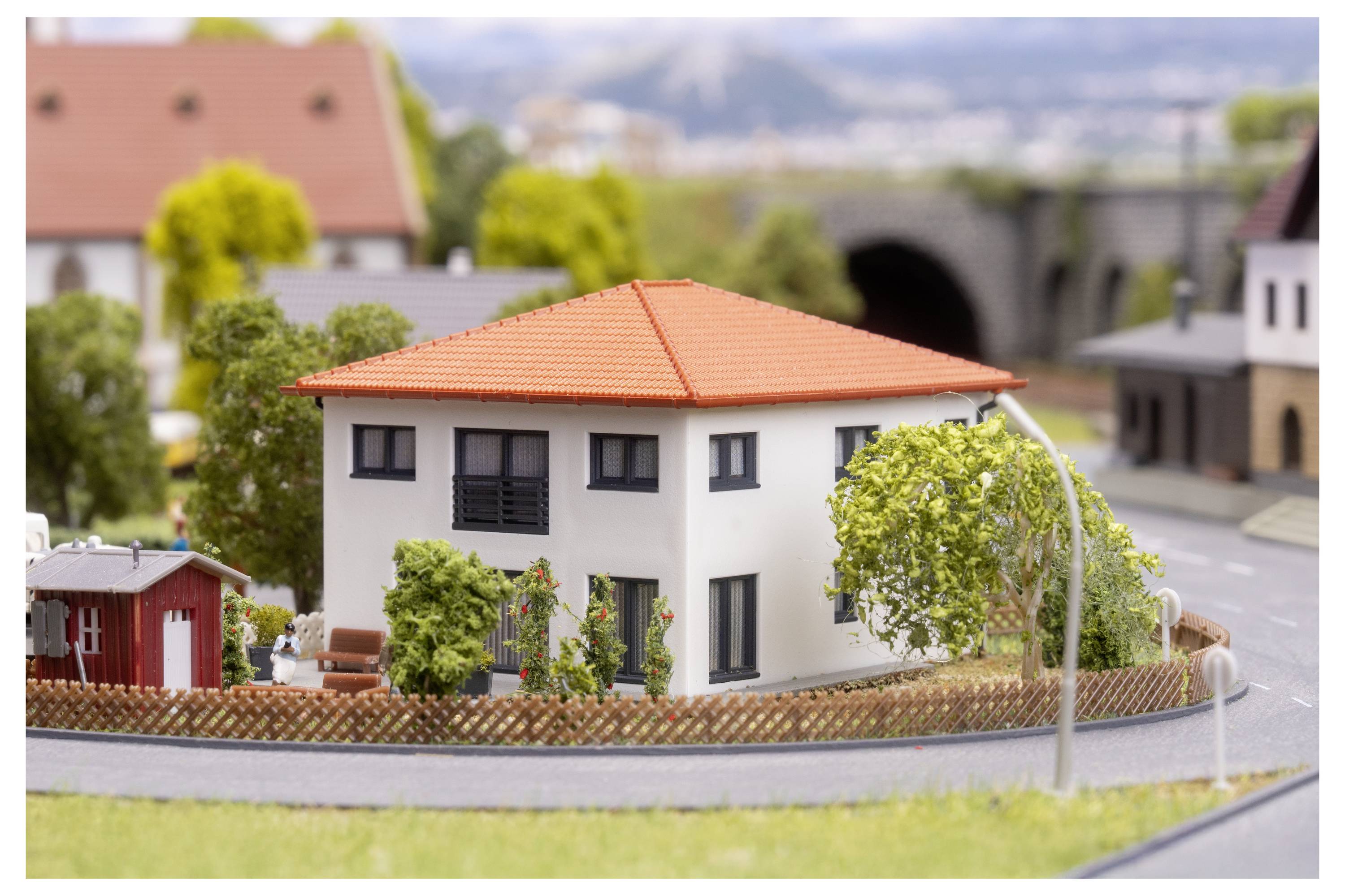 Modell eines modernen zweistöckigen weißen Hauses mit orangefarbenem Dach auf einer gekrümmten Straße, gezeigt in einer Miniatur-Nachbarschaftsausstellung.