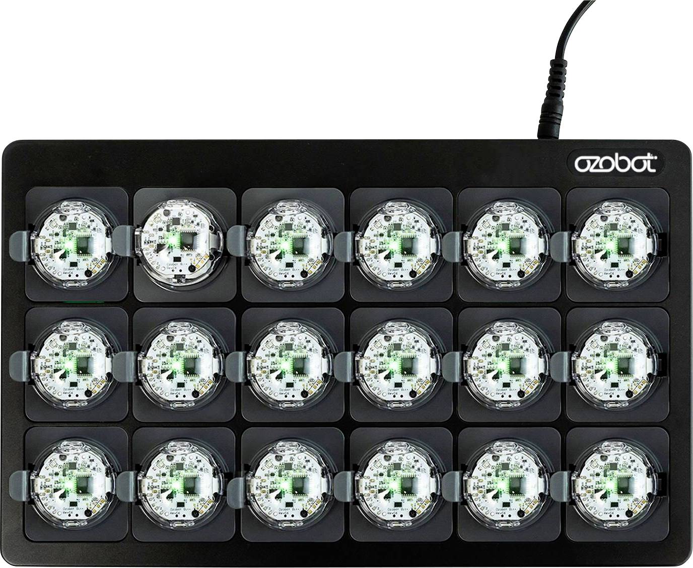 Schwarzes Ozobot-Ladegerät, das 15 kleine Roboter in einem 3×5-Raster hält, mit Stromkabel oben rechts angeschlossen.