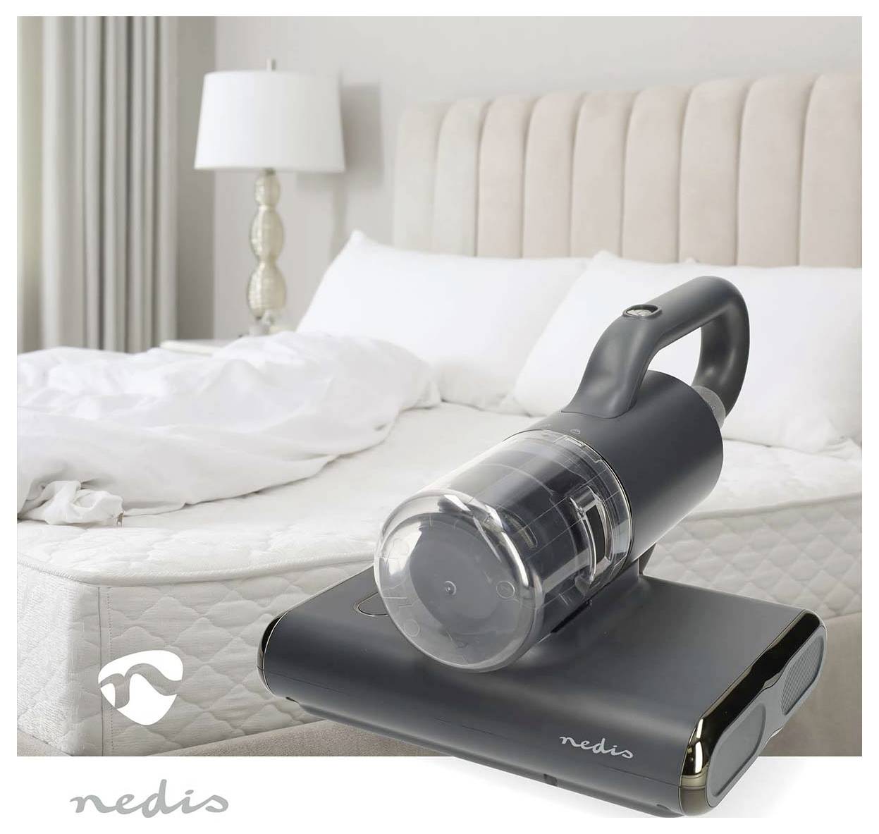 Schwarzer kabelloser tragbarer Staubsauger auf einem Ständer in einem Schlafzimmer, mit einem unmachten Bett und einer Lampe im Hintergrund.