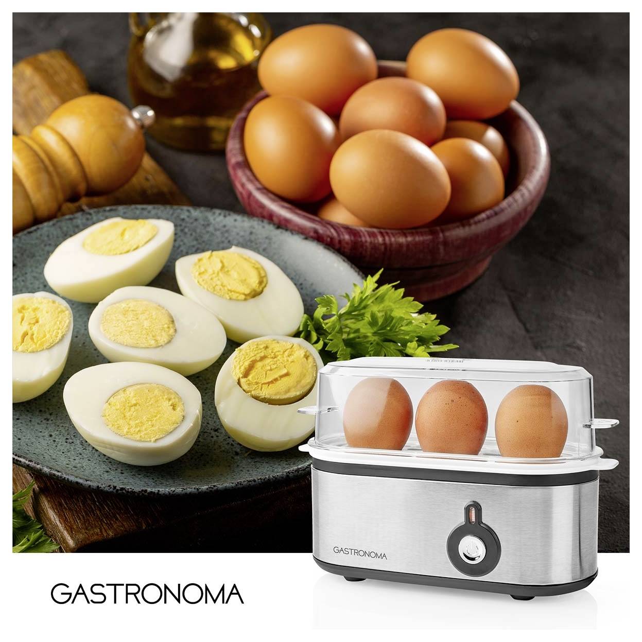 GASTRONOMA Elektro-Eierkocher mit drei Eiern unter einem transparenten Deckel, gezeigt mit gekochten und rohen Eiern auf Tellern und in einer Schüssel dahinter.