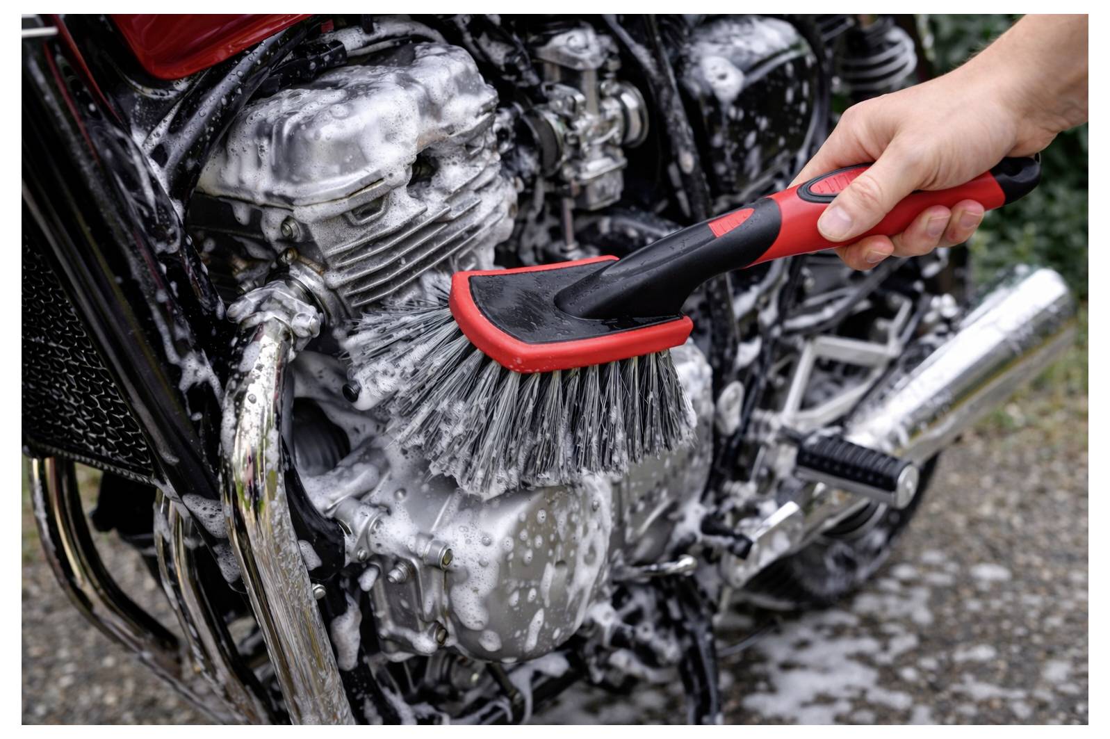 Eine Hand schrubbt einen Motorradmotor und Chromteile mit einer Bürste während einer Wäsche oder Reinigung.