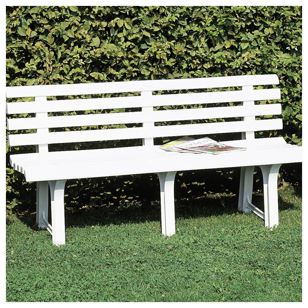 Weiße Parkbank im Freien mit einigen Zeitschriften auf der Sitzfläche, auf Gras vor einer belaubten Hecke aufgestellt.