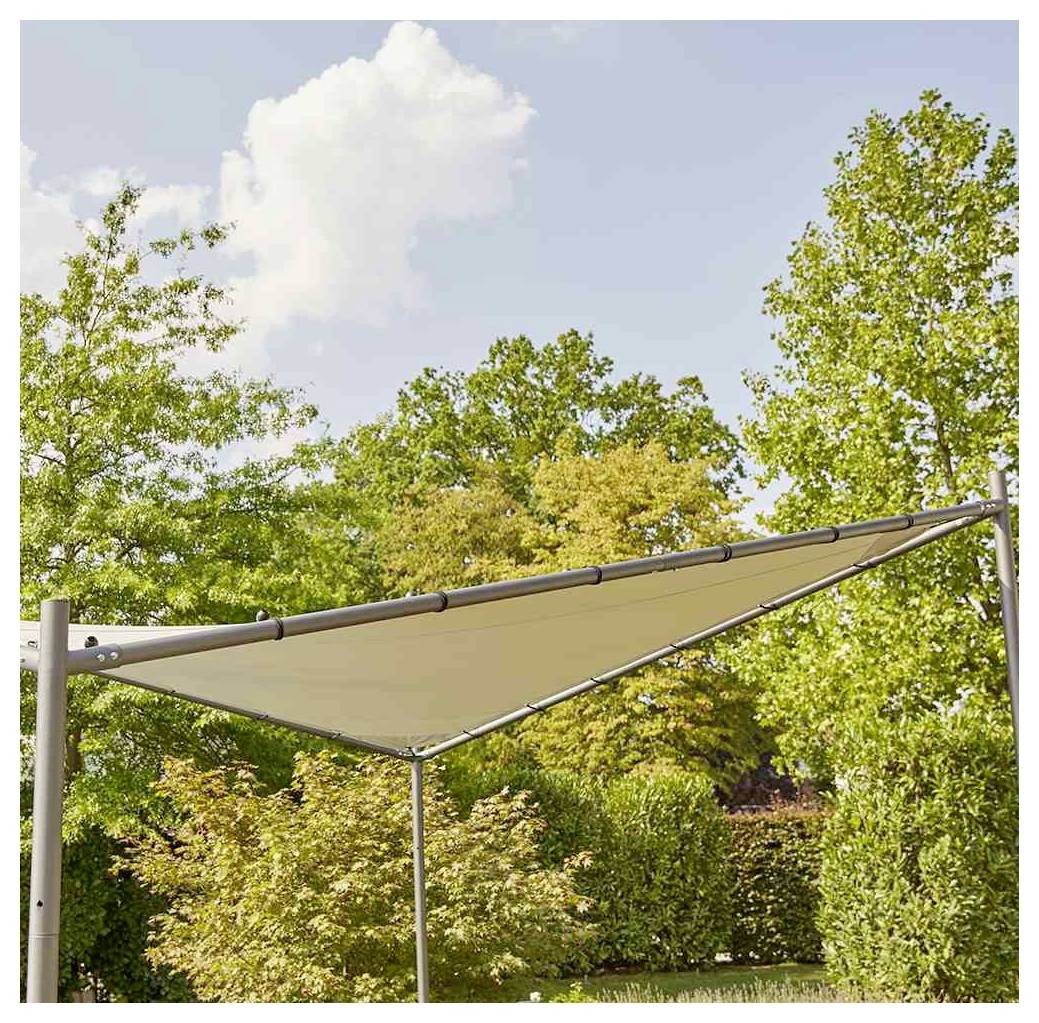 Beiges dreieckiges Sonnensegel, das über einen Garten gespannt ist, mit Bäumen und blauem Himmel im Hintergrund.