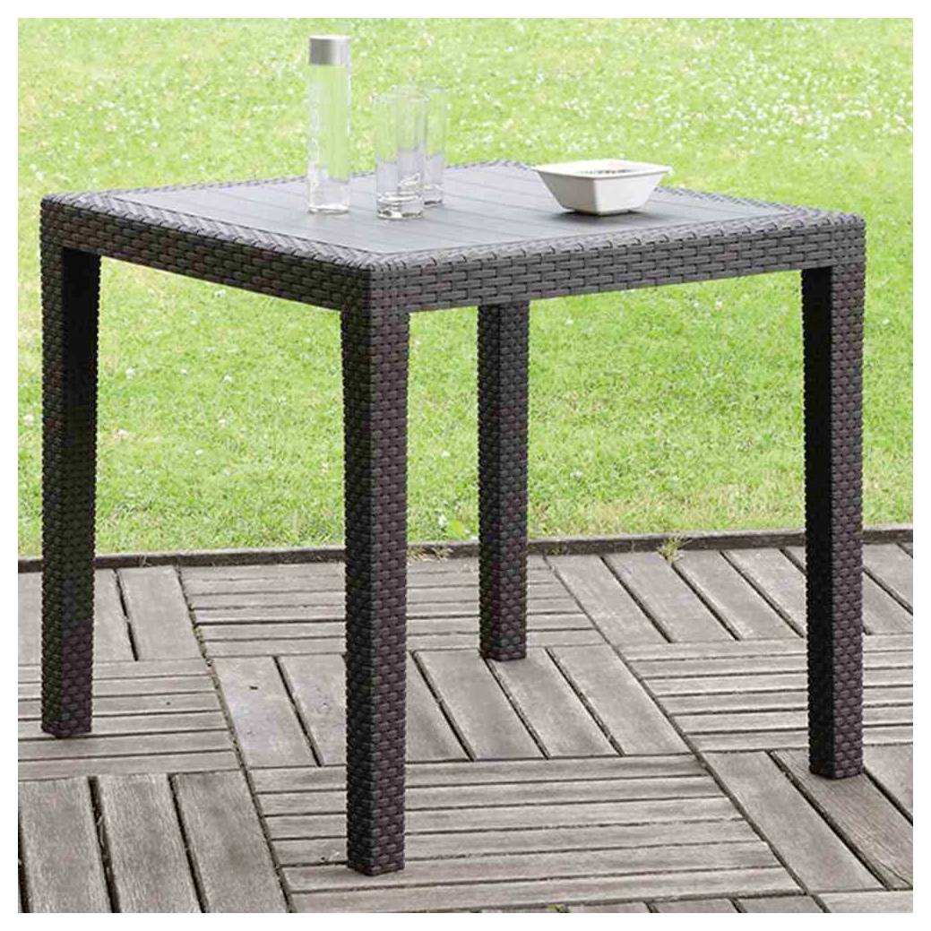 Quadratischer Patio-Tisch im Rattan-Stil für draußen mit Glasplatte, auf dem sich eine Karaffe, Gläser und eine kleine Schüssel auf einer Holzterrasse neben Gras befinden.