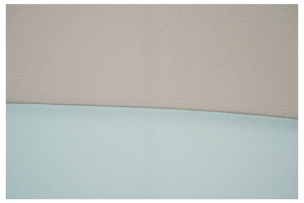 Nahaufnahme einer beige und hellblauen Polsterfläche mit einer horizontalen Naht, die nur abstrakte Stofftexturen und Farben zeigt.