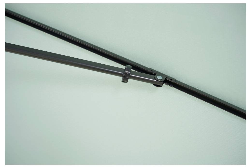 Nahaufnahme eines schwarzen Metallstützarms mit Scharnier vor einem hellgrünen Hintergrund, mit Stecker- und Stangenkupplung.