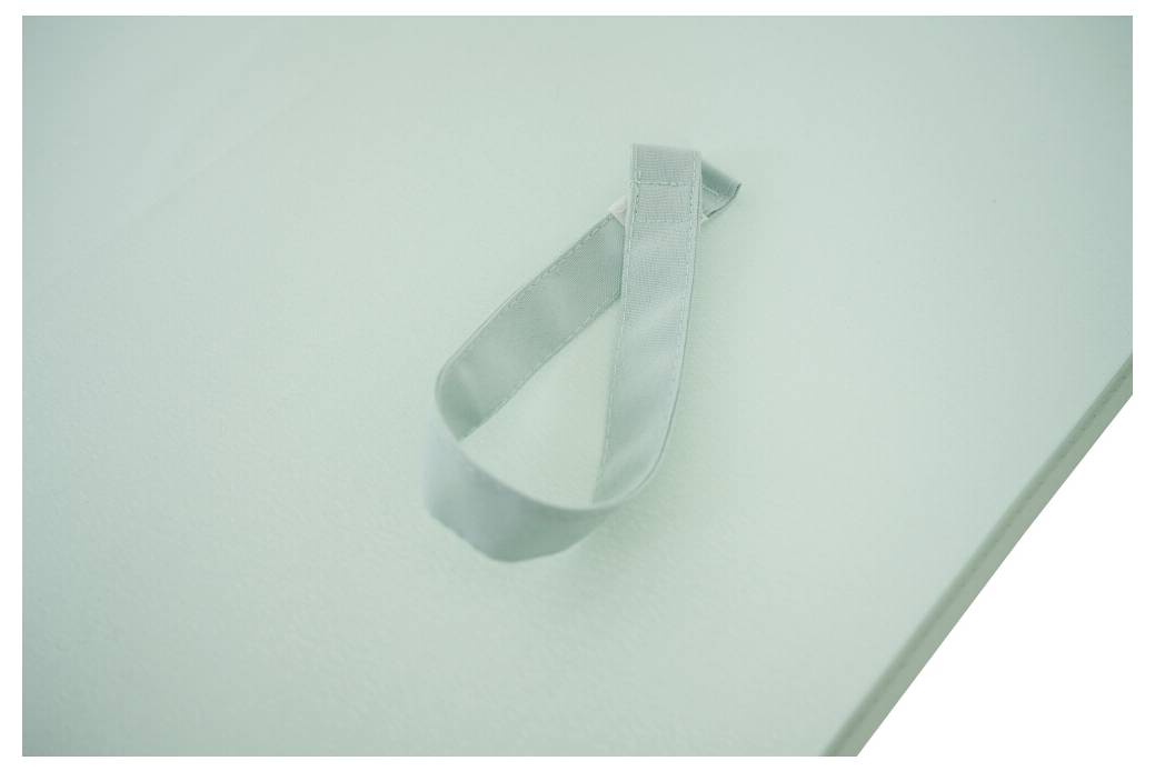 Nahaufnahme einer hellgrünen Oberfläche mit einem kleinen Stoffband oder Riemen mit Schleife in der Nähe der Mitte befestigt.