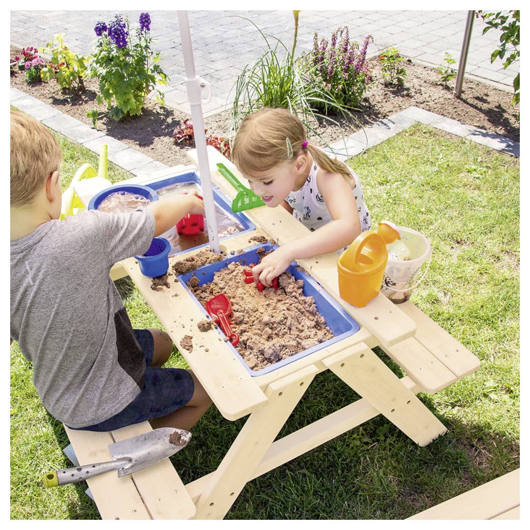 Zwei Kinder spielen mit Sand und Spielzeugwerkzeugen an einem kleinen Sandtisch im Picknick-Stil in einem sonnigen Garten.