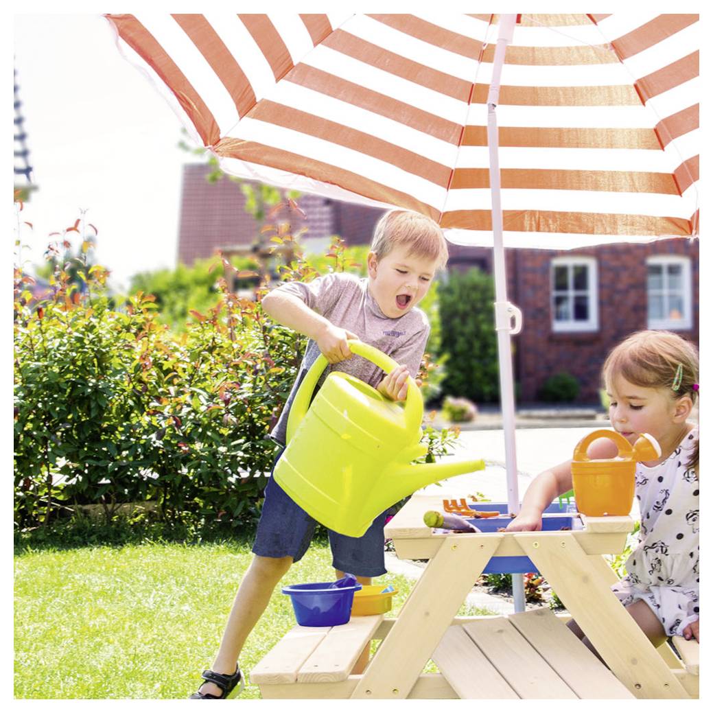 Kinder spielen an einem hölzernen Wassertisch in einem sonnigen Garten, eines gießt aus einer grünen Gießkanne, während ein anderes unter einem gestreiften Regenschirm Wasser schöpft.