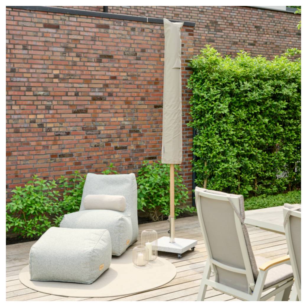 Outdoor-Terrasse mit grauem Liegestuhl, Fußstütze, Sonnenschirm und Essstühlen auf einem Holzdeck neben einer Backsteinmauer und einer grünen Hecke.