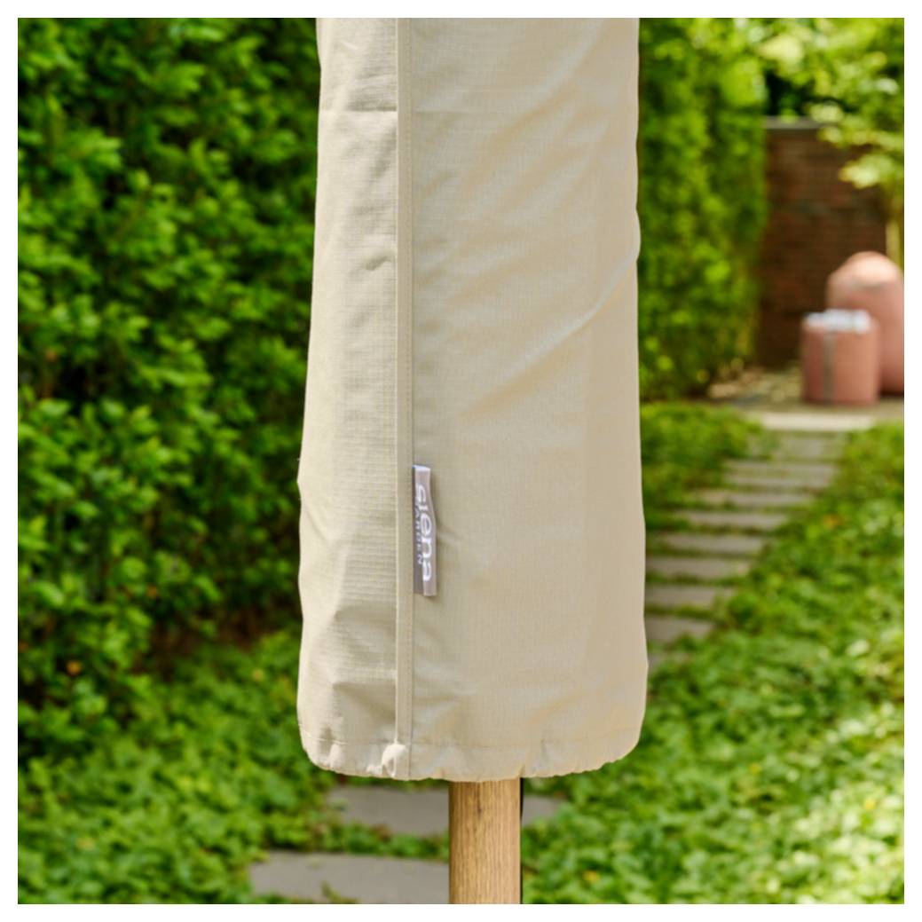 Beige Schutzhülle für Außenschirme auf einem Holzpfosten in einem Garten, mit einem Weg und Hecken im Hintergrund.