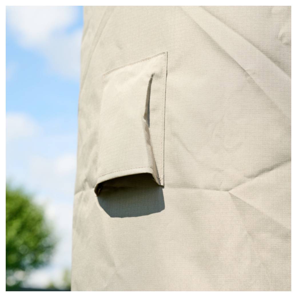 Nahaufnahme einer beigen Zeltplane mit einem kleinen reißverschlossenen Lüftungsschlitz oder einer geöffneten Taschenklappe vor blauem Himmel und unscharfen Bäumen.