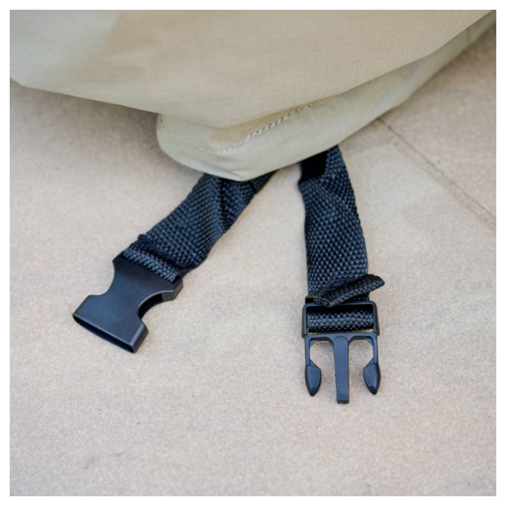 Nahaufnahme eines schwarzen Nylonriemens mit einer Kunststoffschnalle, die unter einem beigen Kissen oder einer Tasche auf einem gekachelten Boden hervorragt.