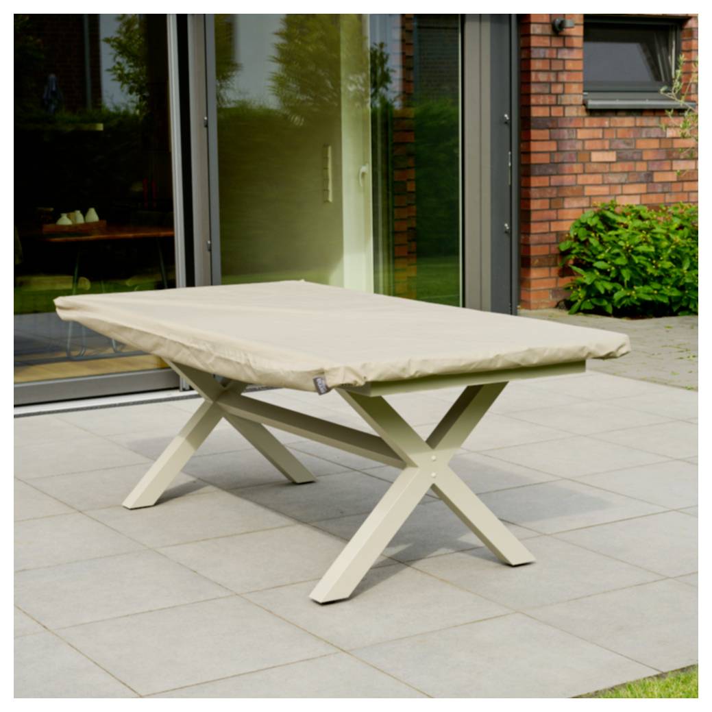 Beige Außentisch mit passender Abdeckung auf einer Terrasse vor einem Backsteingebäude und Glastüren.