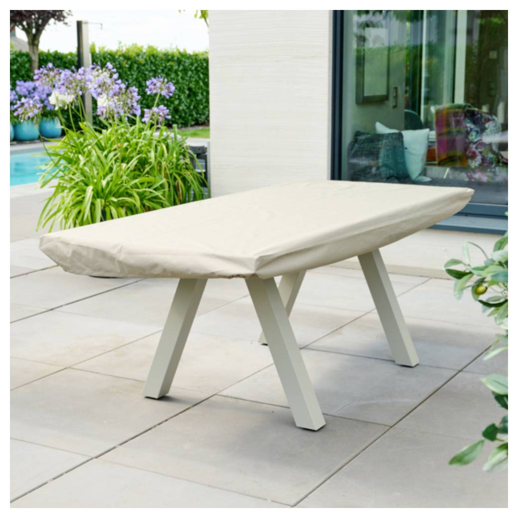 Überdachter Esstisch im Freien auf einer gefliesten Terrasse neben einem Haus, mit beigem Schutzcover und Gartenpflanzen im Hintergrund.