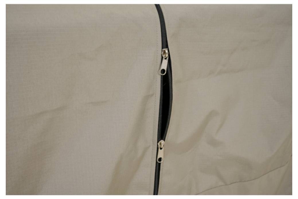 Nahaufnahme einer beige Stoffzelt- oder Taschennaht mit teilweise geöffnetem schwarzem Reißverschluss.