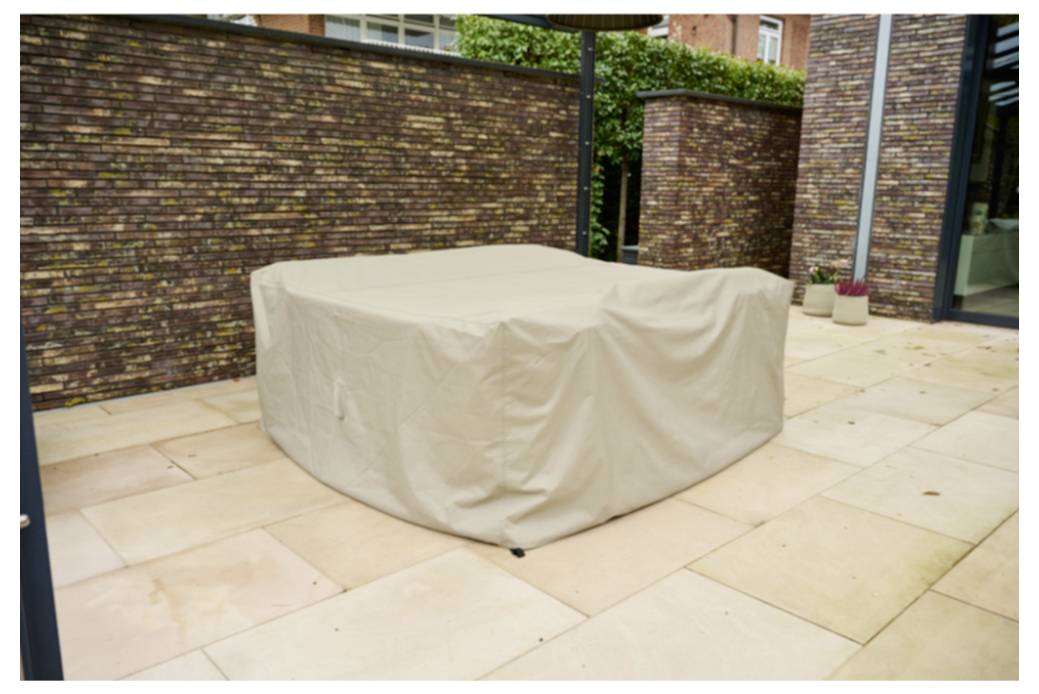 Beige gedeckter Außentisch oder Möbel auf einer gefliesten Terrasse neben Ziegelmauern und einem Hauseingang.