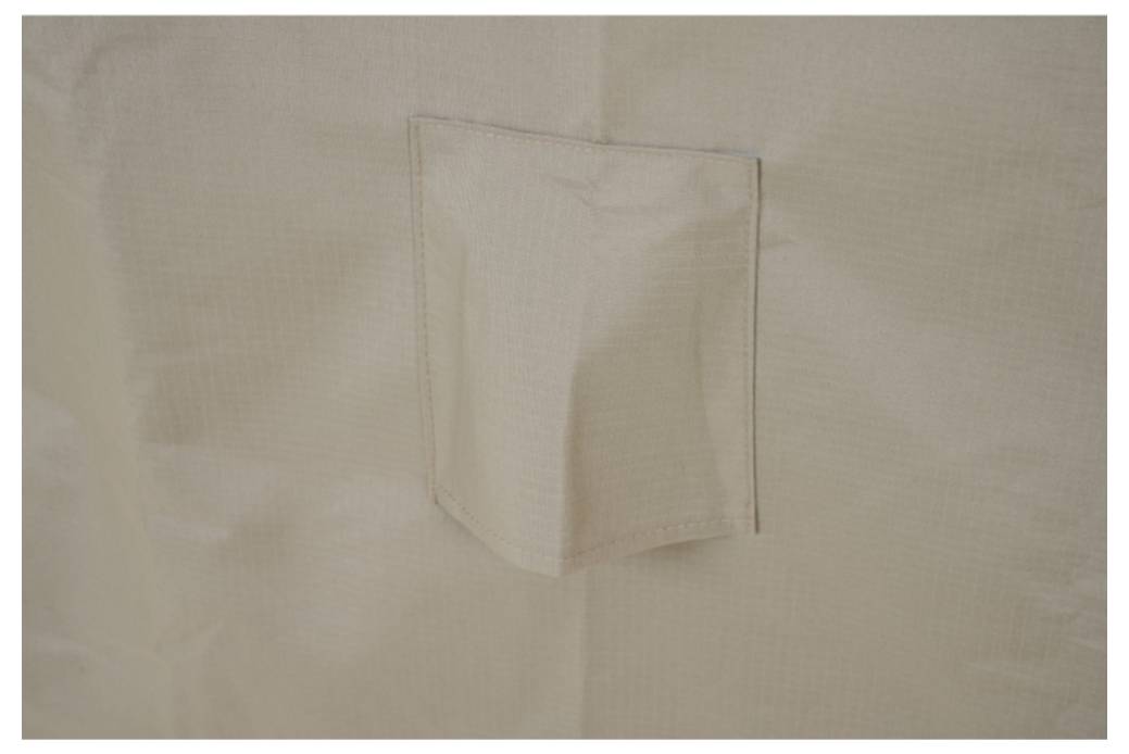 Nahaufnahme eines beigefarbenen Stoffwandpanels mit einer kleinen genähten rechteckigen Klappe oder Tasche in der Mitte.