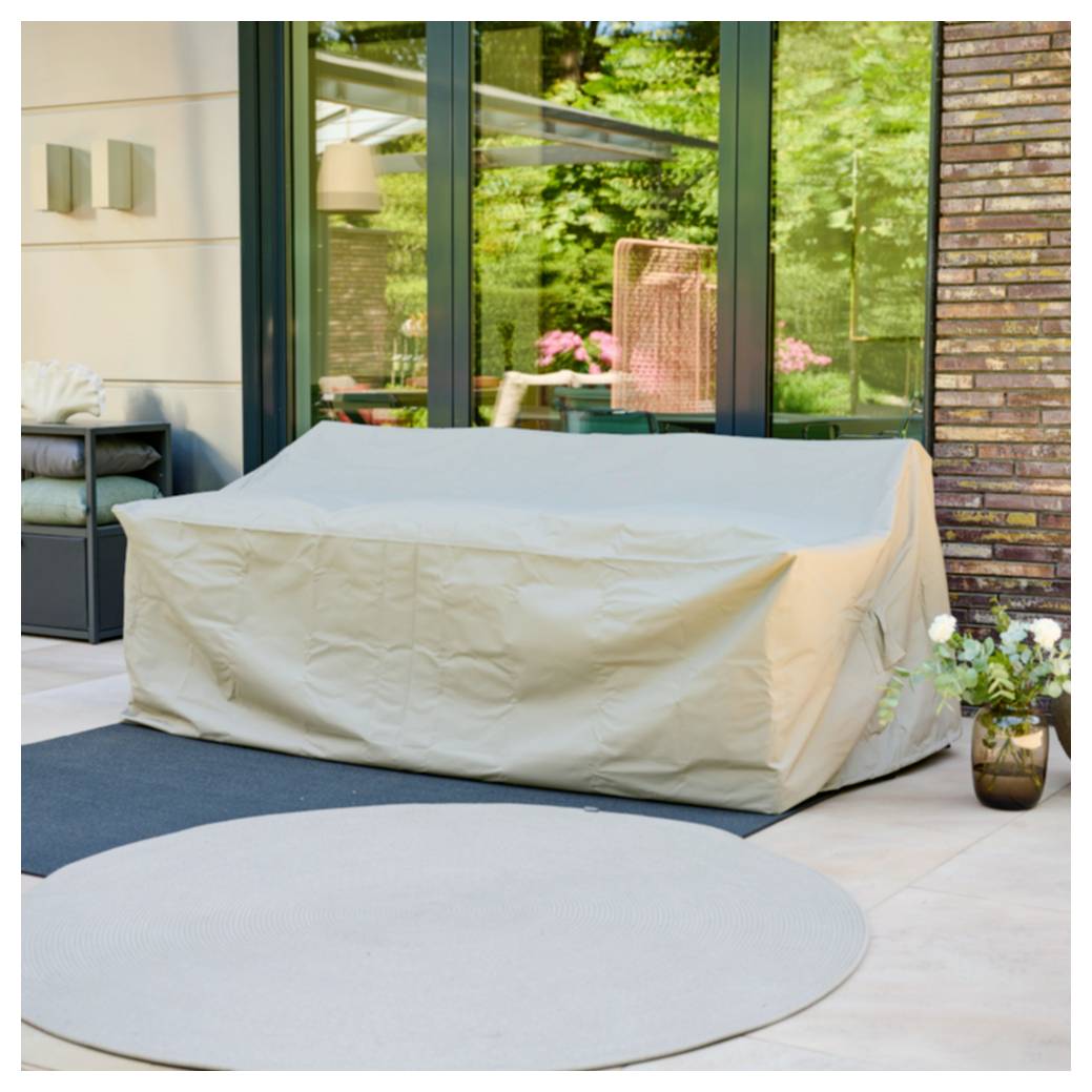 Überdachtes Außensofa auf einer Terrasse neben großen Glastüren, mit einem runden Teppich und Topfblumen im Vordergrund.