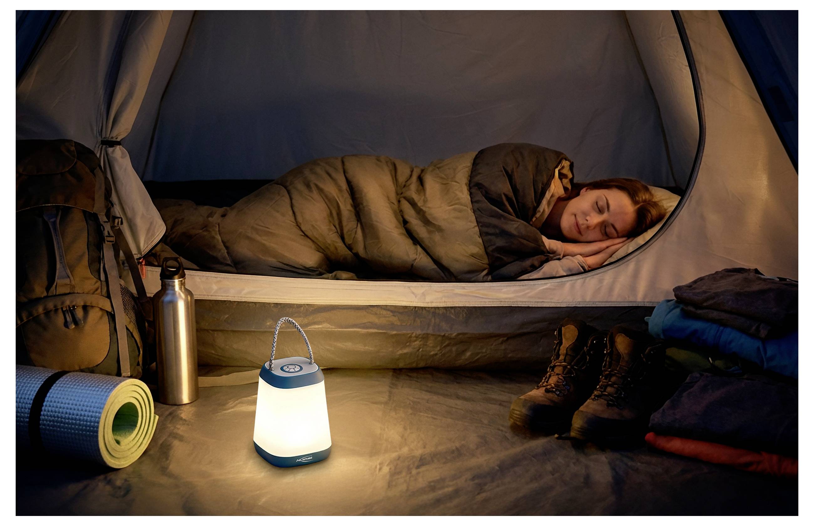 Person schläft in einem Zelt neben einer leuchtenden Laterne, Schlafmatte, Stiefeln und Campingausrüstung, was auf eine Übernachtung beim Camping hinweist.