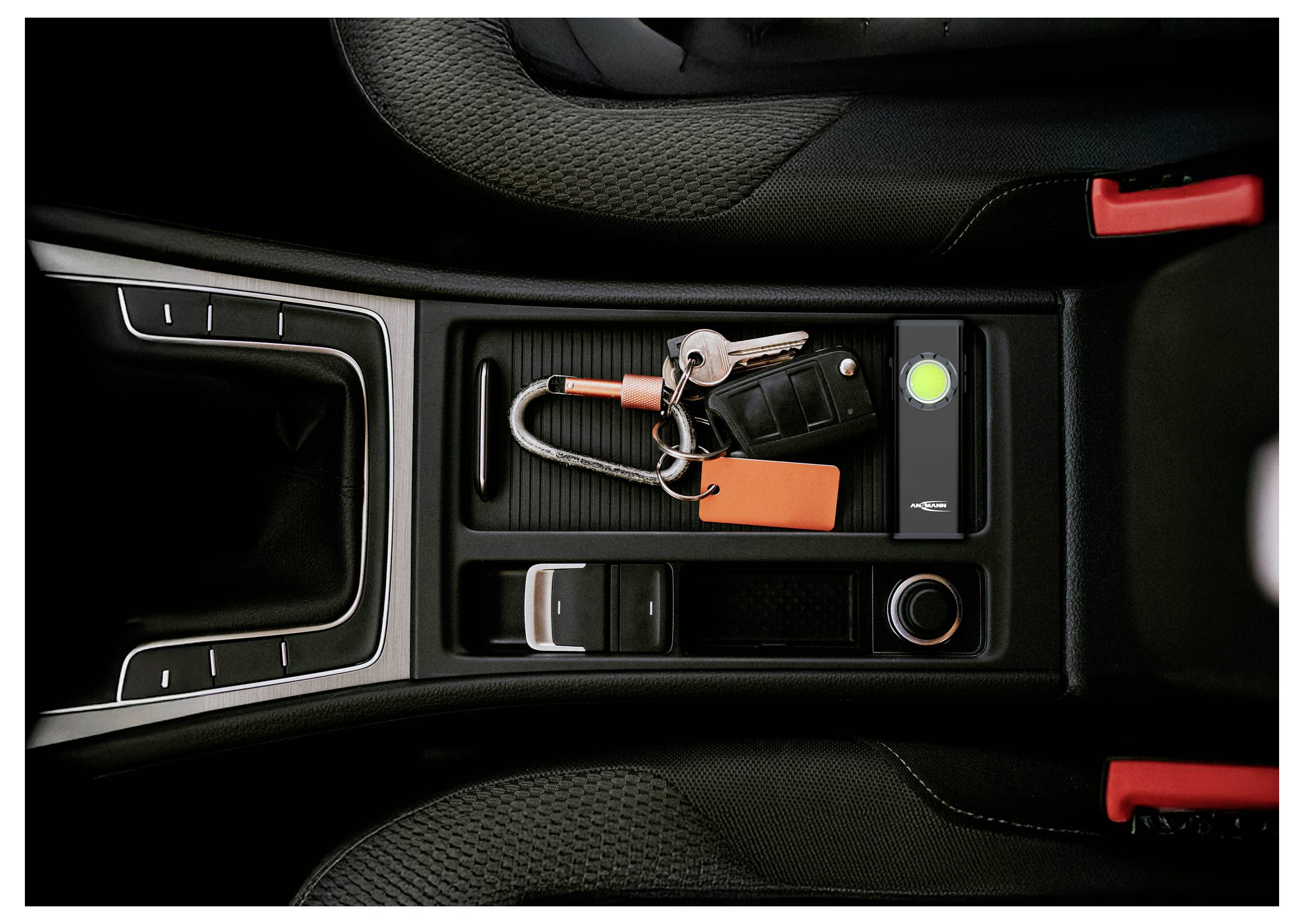 Ablagefach in der Mittelkonsole des Autos mit Autoschlüsseln, einem Schlüsselanhänger und einem orangen Etikett neben einem leuchtenden grünen Anzeigeknopf.