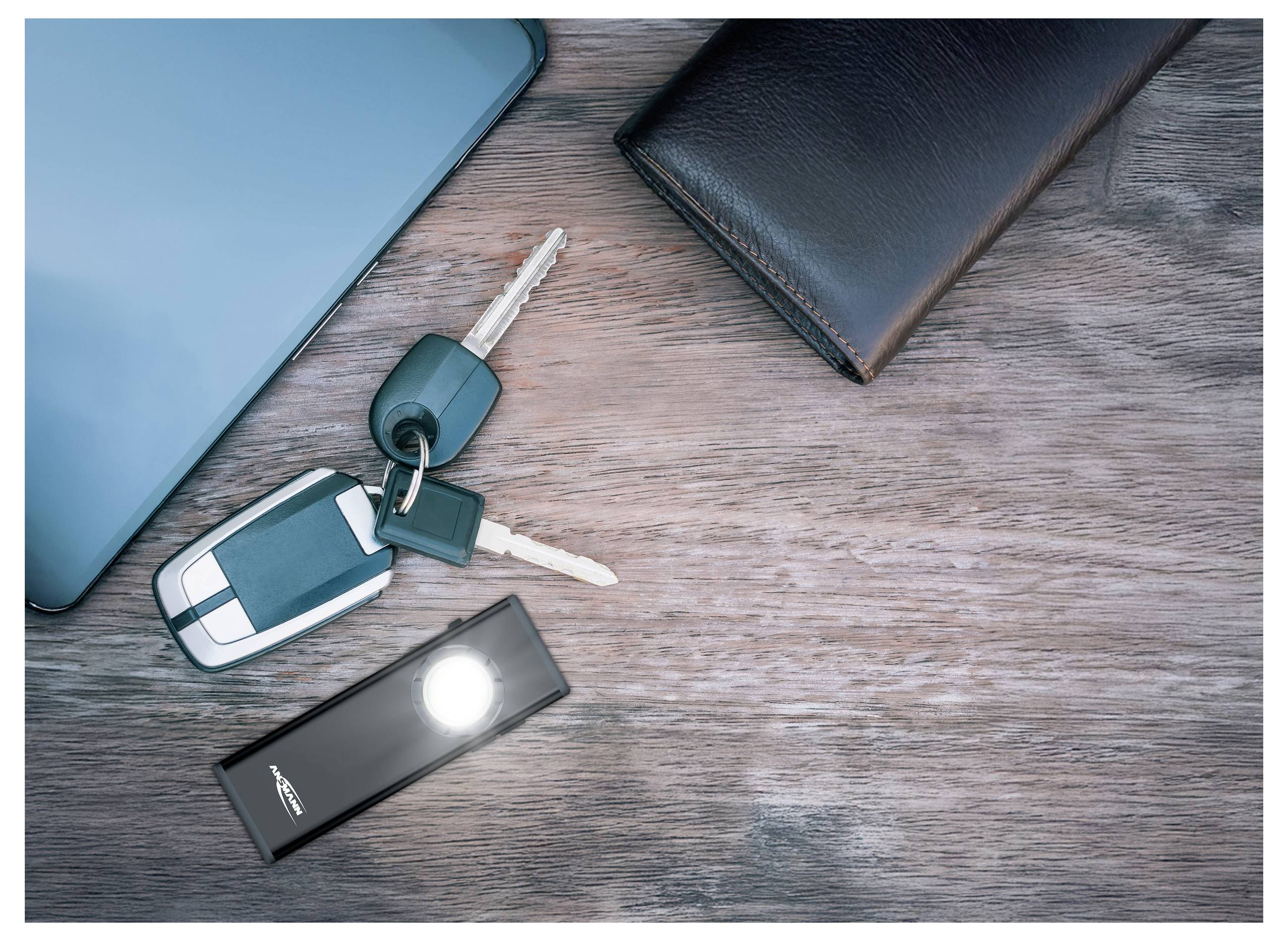 Autoschlüssel, Taschenlampe, Laptop und Geldbörse auf einem Holzschreibtisch, was auf alltägliche Gegenstände oder persönliche Gegenstände hindeutet, die zur Verwendung bereit sind.