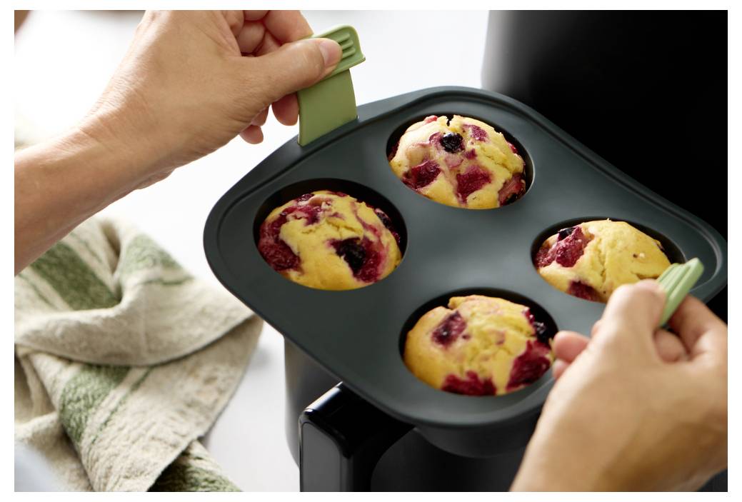 Hände nehmen ein Muffinblech für vier Muffins aus dem Ofen und zeigen gerade gebackene Beerenmuffins, die noch im Blech sind.