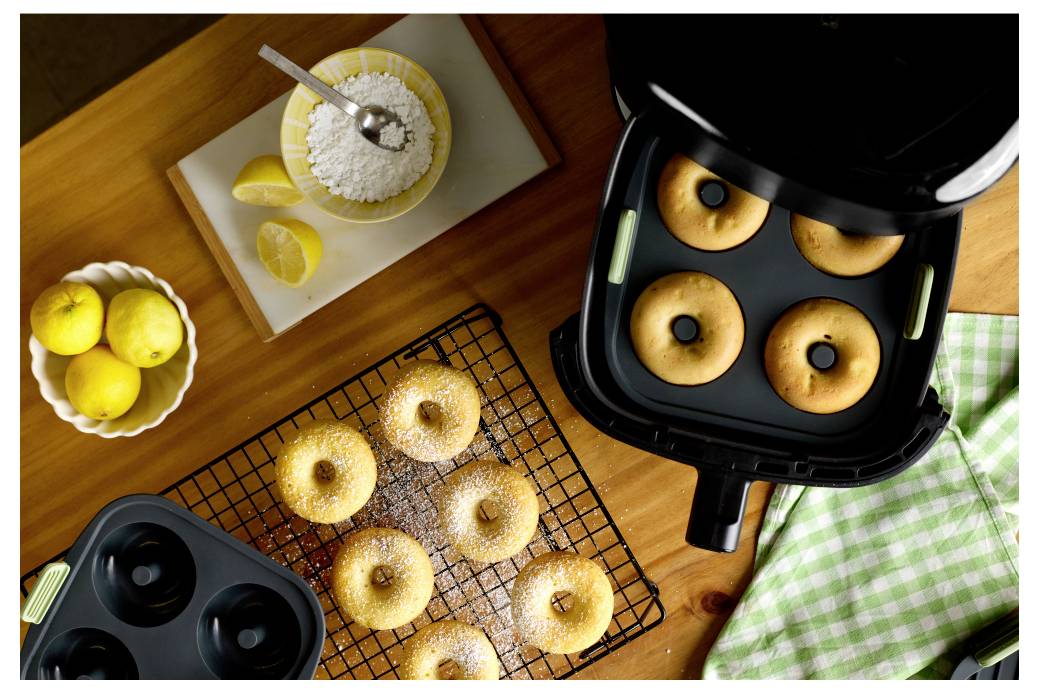 Draufsicht auf Bagels und Beläge mit einer Heißluftfritteuse, die vier Bagels hält, plus Obst, Zucker und Kühlgitter auf einem Holztisch.