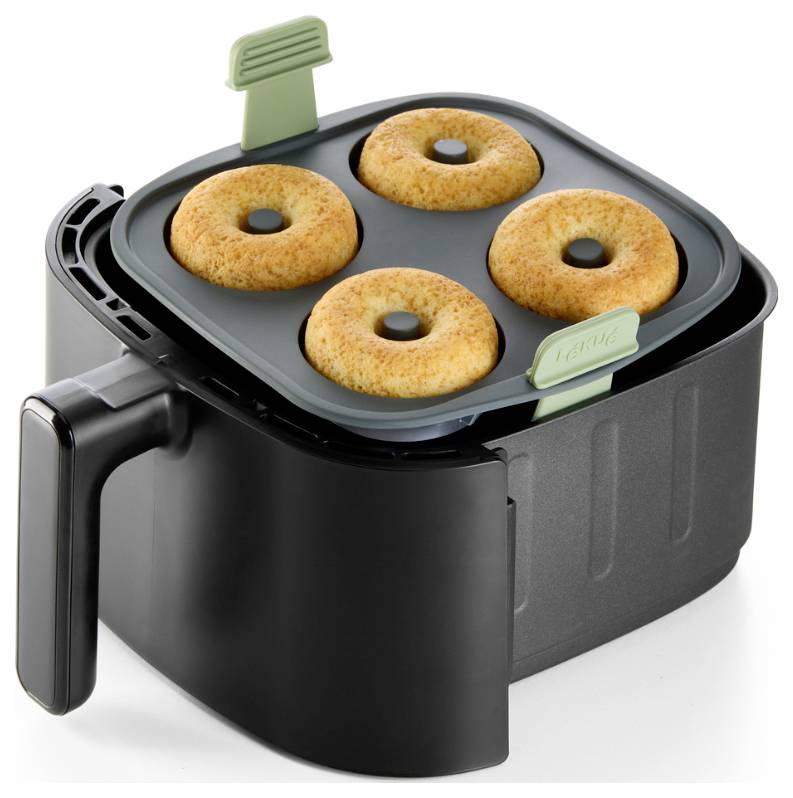 Schwarze Heißluftfritteuse mit Korb-Tablett, auf dem vier gebackene Donuts auf weißem Hintergrund liegen.
