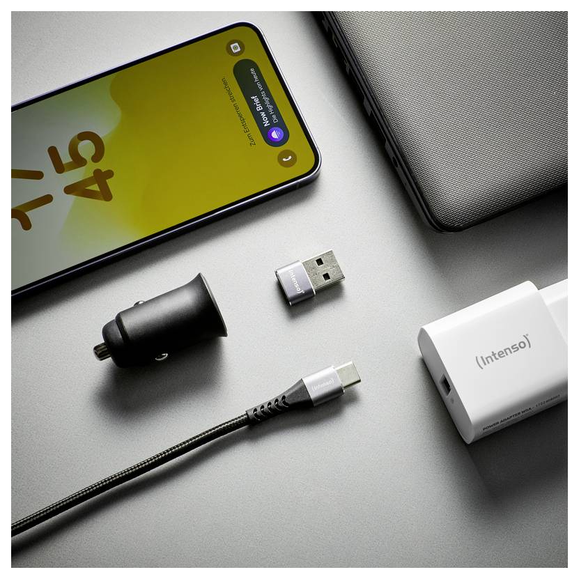 Smartphone, USB-Adapter, Autoladeadapter, Kabel und Powerbank auf einer grauen Oberfläche angeordnet, was auf Ladezubehör für Mobilgeräte hindeutet.