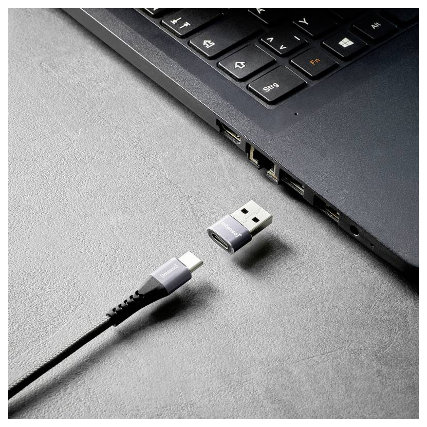 USB-C-Kabel mit separatem Adapterstecker, das neben den Anschlüssen an der Seite eines Laptops auf einer grauen Oberfläche dargestellt ist.