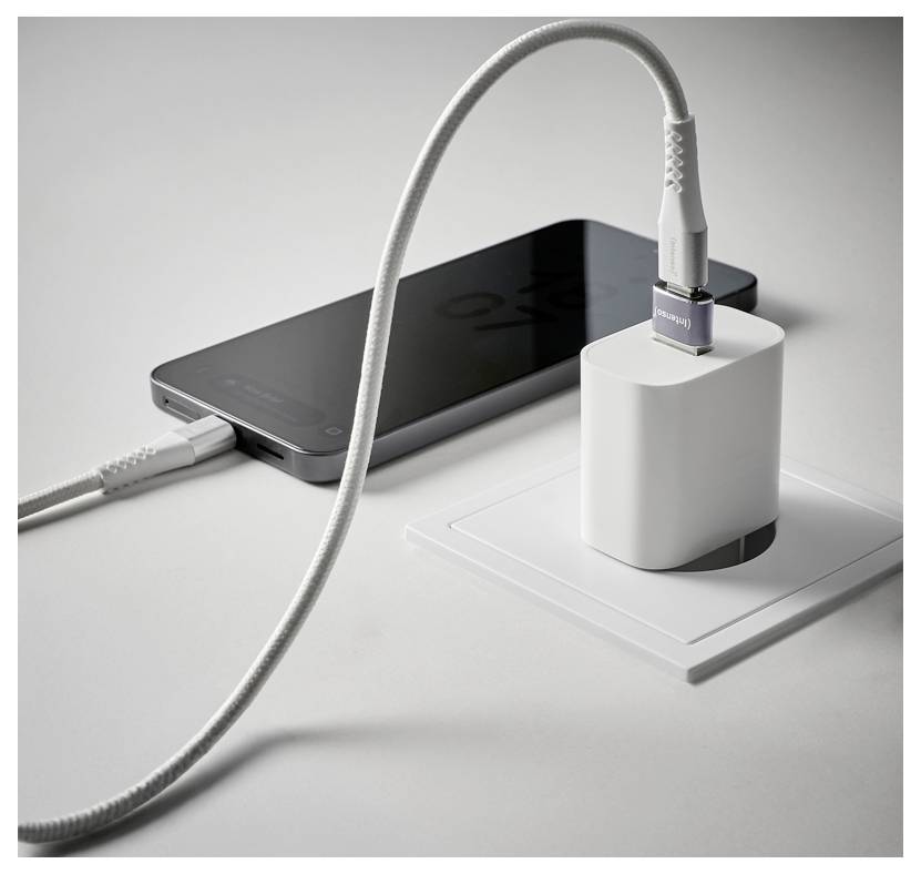 Ein Smartphone wird mit zwei weißen Kabeln geladen, die mit einem Wandstecker-Adapter auf einer weißen Oberfläche verbunden sind.