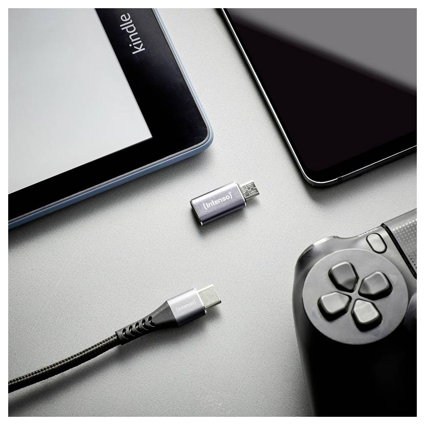 USB-C-Adapter und Kabel neben einem Tablet, Smartphone und Game-Controller auf einer grauen Oberfläche, was auf Geräteaufladung oder Konnektivität hindeutet.