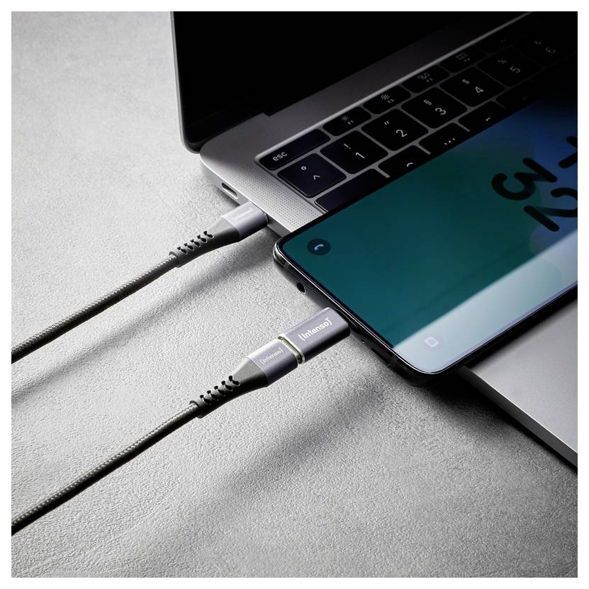 Nahaufnahme eines Laptops und eines Smartphones, die durch zwei Kabel verbunden sind und Geräteladung oder Datentransfer suggerieren.