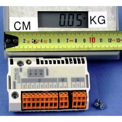 Ein kompaktes elektronisches Modul mit Anschlussverbindern wird neben einem Lineal und einer digitalen Waage mit der Anzeige 0,05 KG gezeigt, was seine Größe und sein Gewicht angibt.