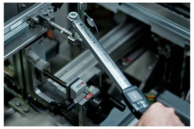 Nahaufnahme eines digitalen Drehmomentschlüssels, der beim Zusammenbau einer Industriemaschine verwendet wird, mit einer Hand, die eine Befestigung anpasst.