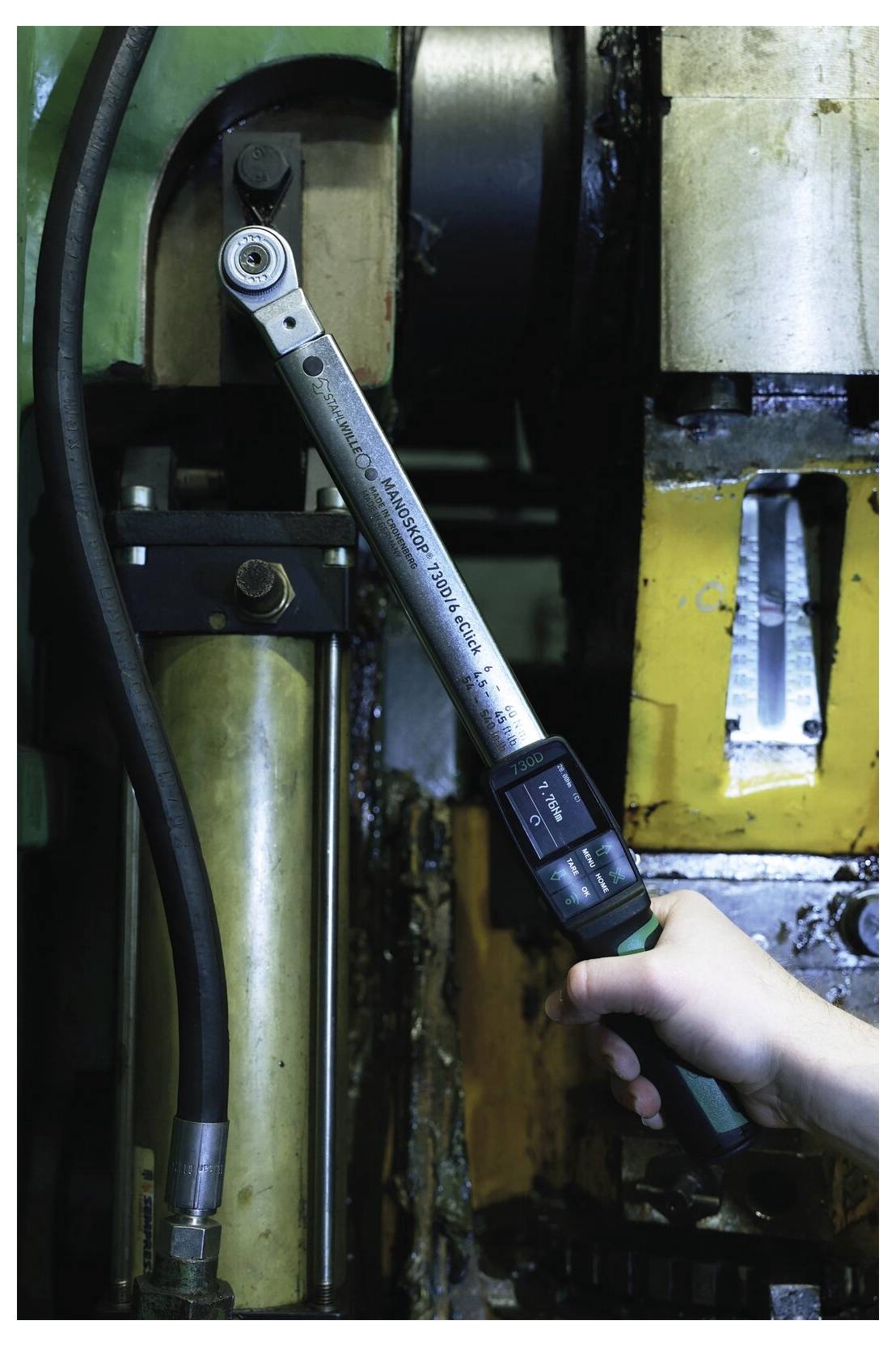 Hand benutzt einen Drehmomentschlüssel an einer Industriemaschine, zieht einen Bolzen in einer metallischen mechanischen Baugruppe fest.