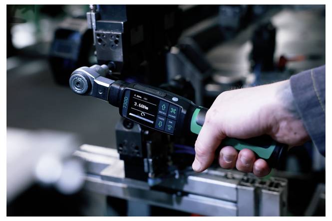 Nahaufnahme eines Arbeiters, der einen digitalen Drehmomentschlüssel an einer Industriemaschine verwendet, mit einem Display, das Messdaten anzeigt.