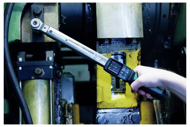 Eine Hand benutzt einen digitalen Drehmomentschlüssel, um einen großen Bolzen an einer Industriemaschine festzuziehen.