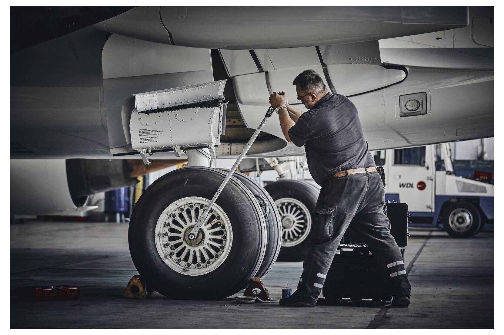 Mechaniker mit einem langen Schraubenschlüssel, der ein Flugzeuglfahrwerk-Rad in einer Hangarwerkstatt wartet.