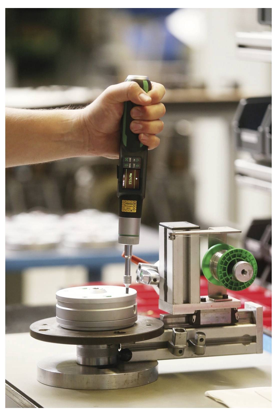 Eine Person nutzt einen tragbaren Elektroschraubendreher an einer kleinen Maschinenvorrichtung in einer Werkstatt, was auf Montage- oder Präzisionsreparaturarbeiten hindeutet.