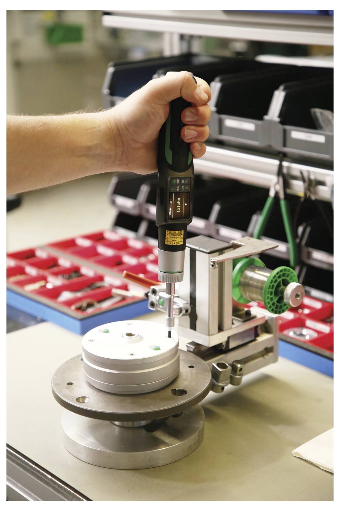Eine Hand hält einen Präzisionsschraubendreher oder eine Bohrmaschine, um eine kleine Metallbefestigung auf einer Werkbank in einer Werkstatt anzupassen.