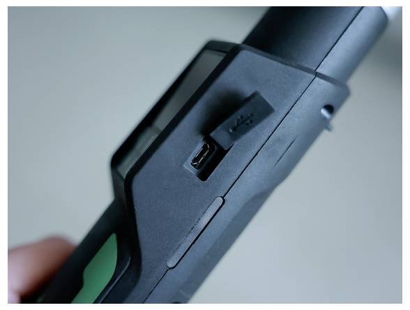 Nahaufnahme eines schwarzen elektronischen Geräts mit einem Micro-USB-Ladeanschluss und einem Schiebeschalter, wobei eine Hand es hält.